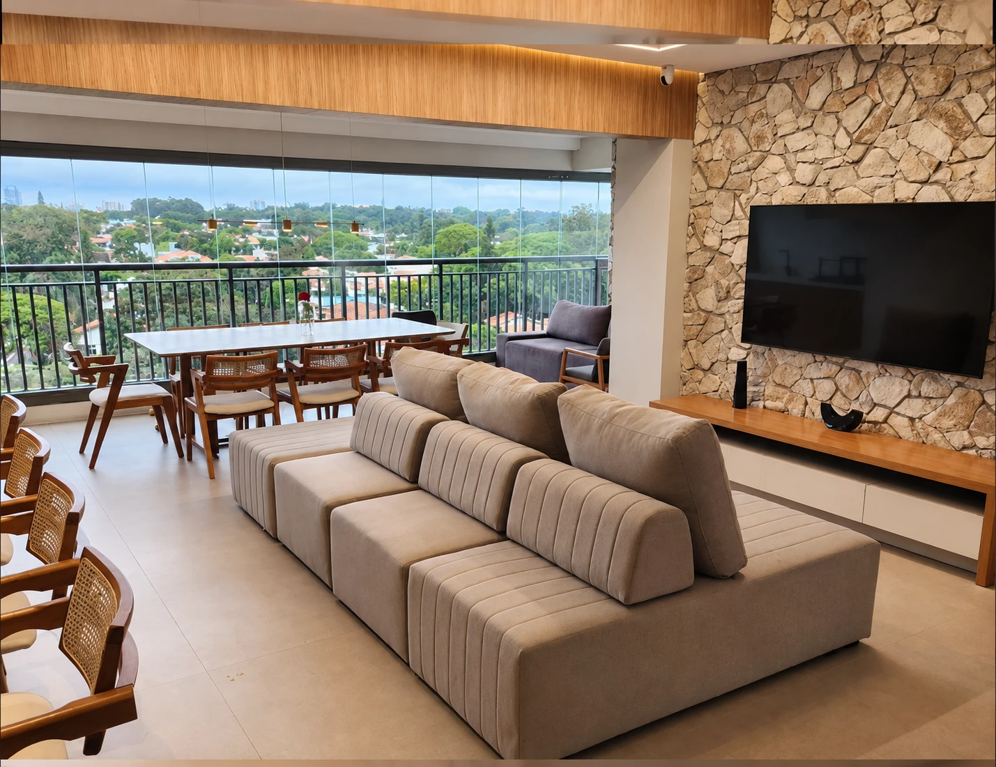Sala com sofá bege, varanda e parede de pedra